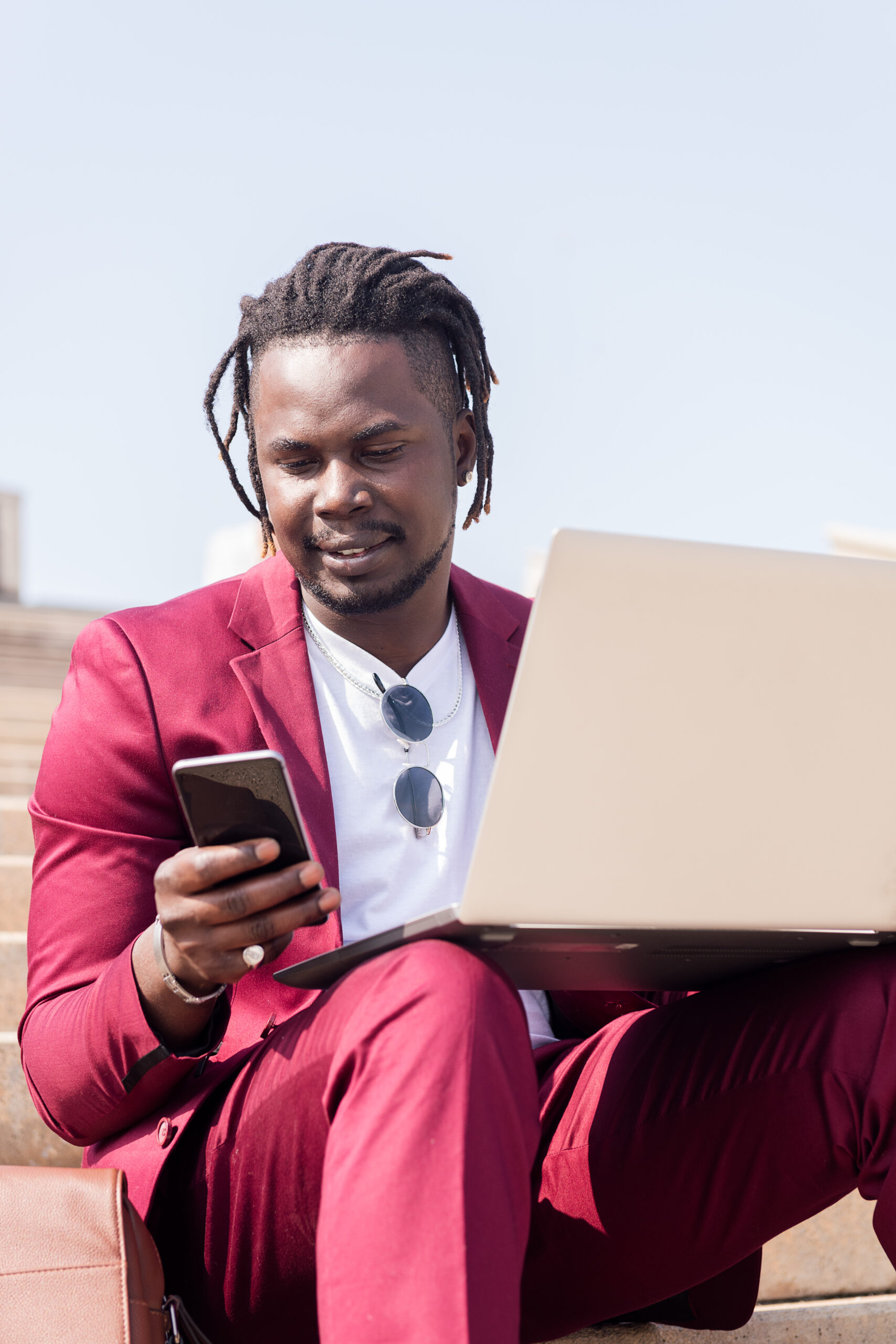 stylish man working outdoors with laptop and phone